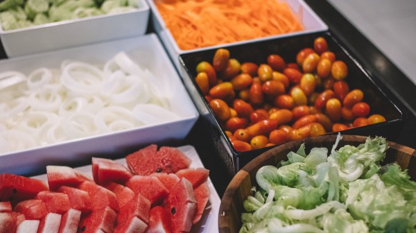 Bowls of sliced watermelon, lettuce, onions, tomatoes, cucumbers, and shredded carrots.