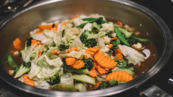 Mixed vegetables, including broccoli and carrots, cooked in a metal pan.