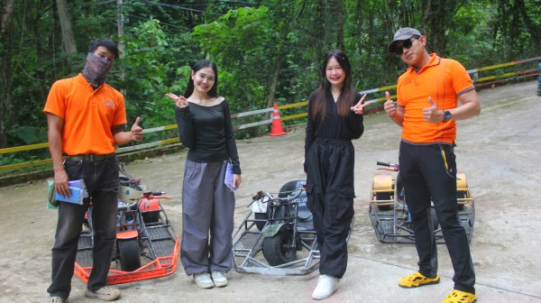 Four people posing with go-karts on a forest path.