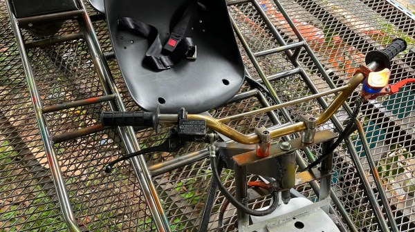 Metal frame vehicle with two black seats and a front wheel on mesh platform.