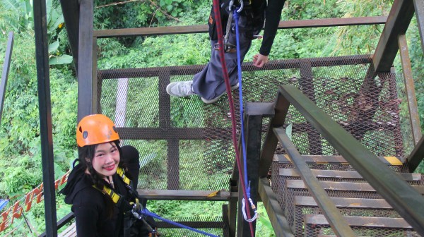 Two people on a metal staircase in harnesses and helmets, surrounded by lush greenery.