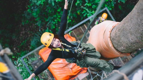 Person in yellow helmet zip-lining through trees, smiling at camera.