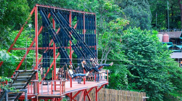People seated on a giant swing ride surrounded by lush green trees.