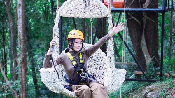 Person on a hanging swing with harness in a forested area, wearing safety gear.